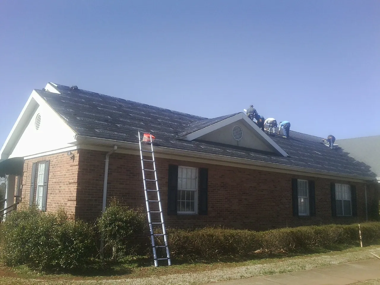 Crew tearing shingles off a brick ranch roof with a ladder set — Emergency Roof Repair work by our crew in Walkerton