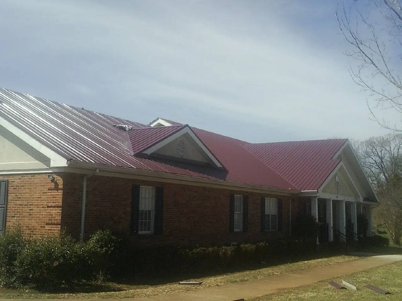Red metal roof with gabled entries on a long brick building, from a Hail Damage Roof Repair job in Walkerton