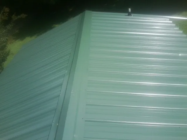 New green metal panels meeting at the ridge of a roof — Flat Roof Repair work by our crew in Walkerton