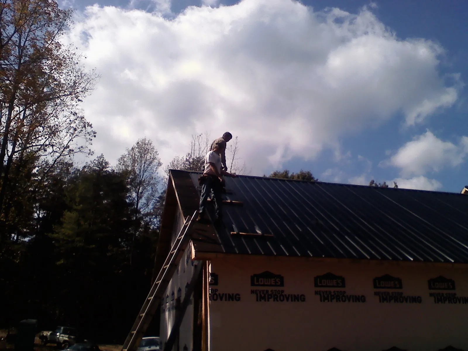 Roofer fastening dark metal panels high against a cloudy sky, from a Roof Inspection job in Walkerton
